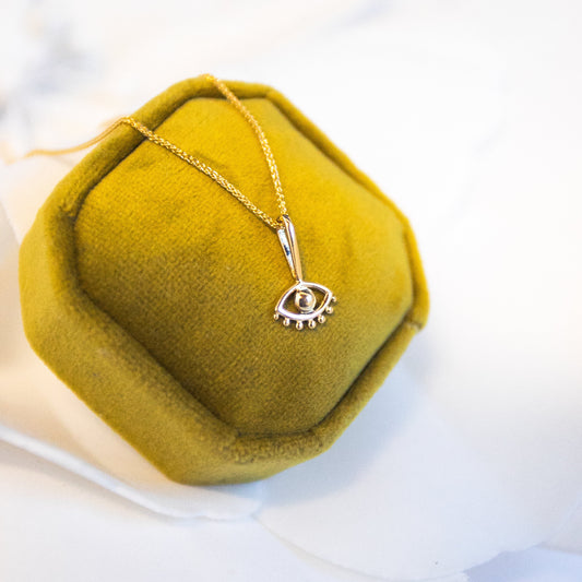 Gold necklace with a pendant on a green cushion against a white background